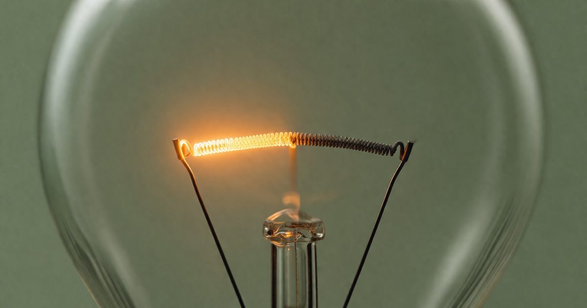 Gros plan macro d'un filament d'ampoule à moitié incandescent et à moitié éteint, métaphore de l'énergie cognitive qui s'épuise